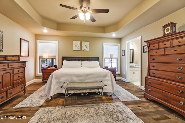 bedroom featuring dark hardwood / wood-style flooring, ensuite bathroom, ceiling fan, and a tray ceiling