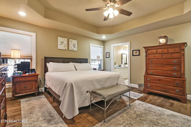 bedroom with a tray ceiling, ensuite bathroom, dark hardwood / wood-style flooring, and ceiling fan