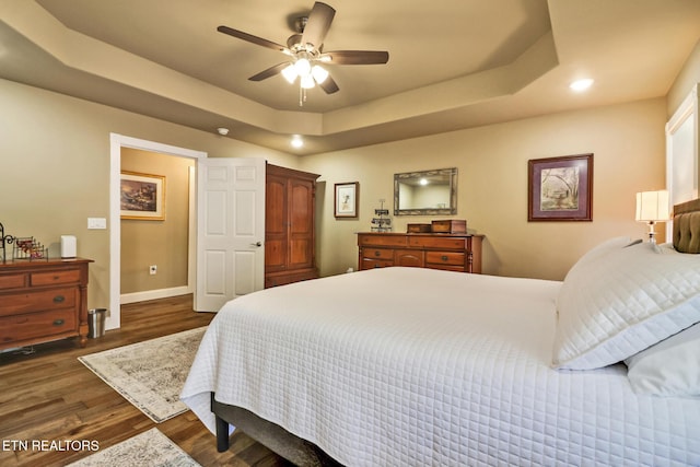 bedroom with a tray ceiling, ceiling fan, and dark wood-type flooring