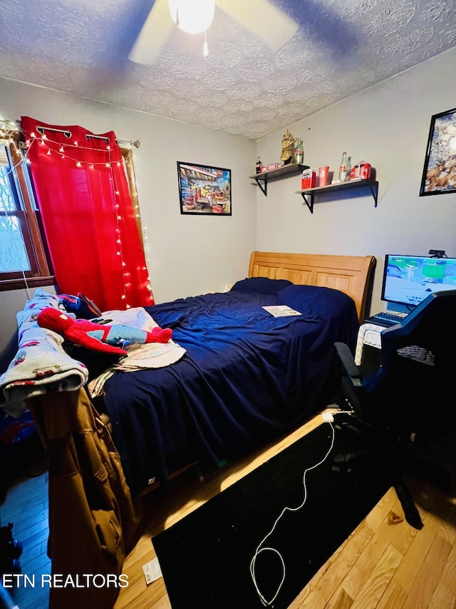 bedroom with hardwood / wood-style floors, ceiling fan, and a textured ceiling