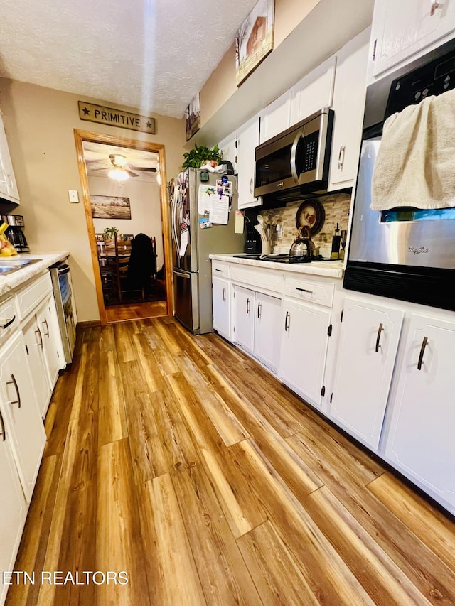 kitchen with white cabinetry, stainless steel appliances, backsplash, a textured ceiling, and light wood-type flooring