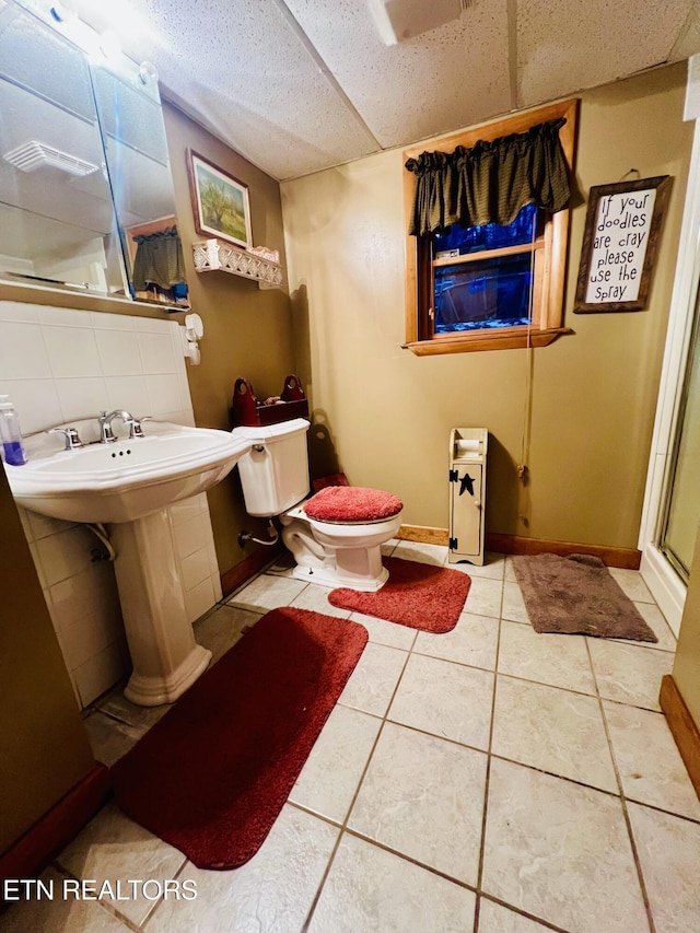 bathroom with a paneled ceiling, tile patterned flooring, toilet, tasteful backsplash, and a shower with shower door