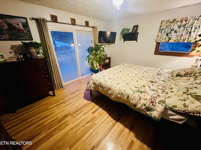 bedroom with hardwood / wood-style floors, a textured ceiling, and access to outside