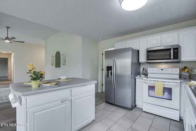 kitchen featuring a textured ceiling, stainless steel appliances, a kitchen island, white cabinetry, and ceiling fan