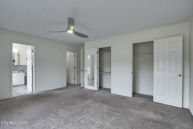 unfurnished bedroom featuring ensuite bathroom, light carpet, multiple closets, and ceiling fan