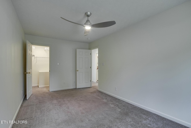 unfurnished bedroom with a textured ceiling, a closet, a walk in closet, ceiling fan, and light carpet