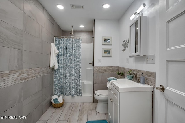 bathroom with tile walls, toilet, walk in shower, and vanity