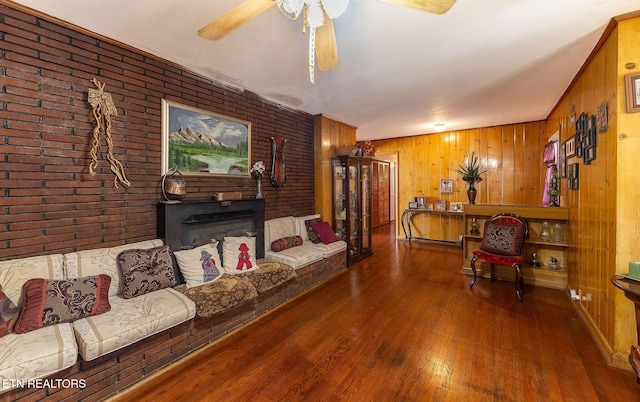 living room with brick wall, ceiling fan, a wood stove, and hardwood / wood-style flooring