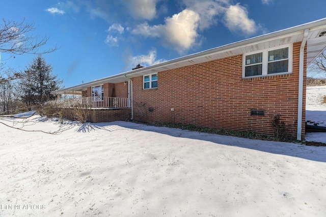 snow covered rear of property featuring covered porch