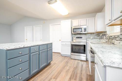 kitchen with appliances with stainless steel finishes, white cabinetry, blue cabinetry, backsplash, and vaulted ceiling