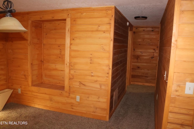 hallway featuring wooden walls, dark carpet, and a textured ceiling