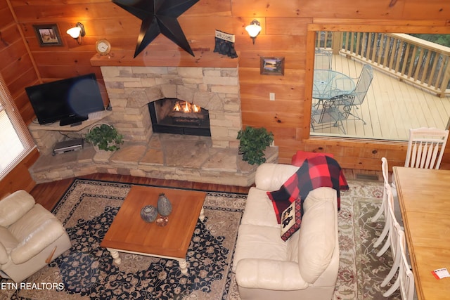 living room featuring a stone fireplace and wood walls