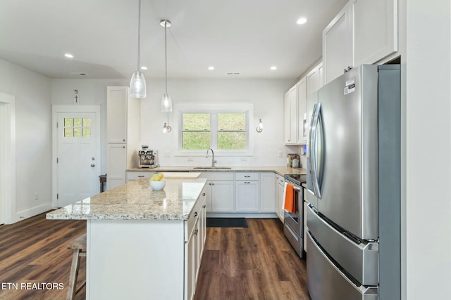 kitchen with stainless steel appliances, sink, white cabinets, a kitchen island, and pendant lighting