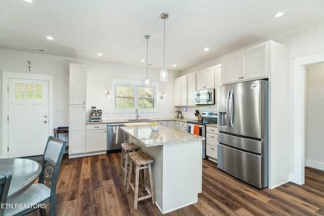 kitchen featuring white cabinets, light stone counters, a kitchen island, pendant lighting, and appliances with stainless steel finishes