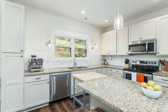 kitchen featuring hanging light fixtures, backsplash, white cabinets, appliances with stainless steel finishes, and sink