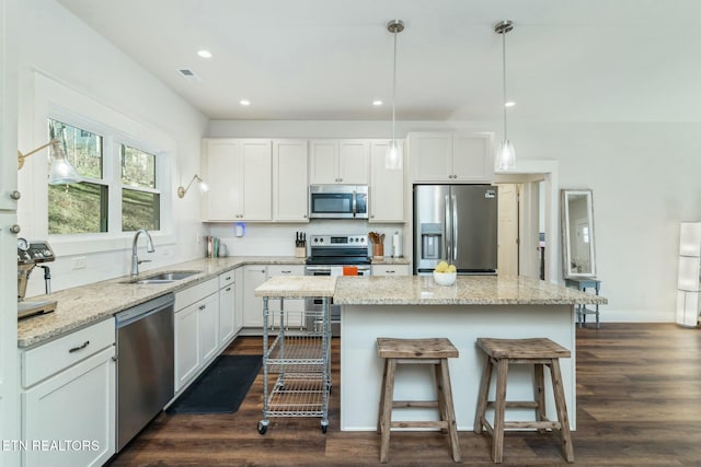 kitchen with pendant lighting, a kitchen island, white cabinets, appliances with stainless steel finishes, and sink