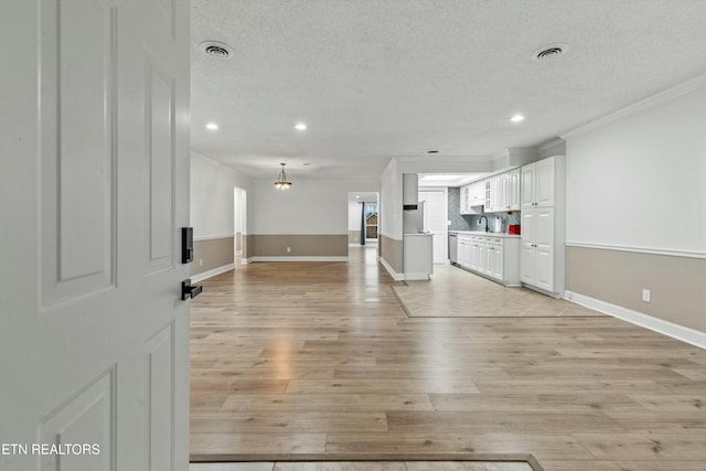 unfurnished living room featuring a textured ceiling, light wood-type flooring, and ornamental molding