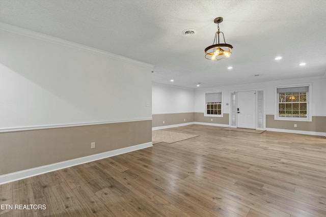 unfurnished living room with a textured ceiling, light wood-type flooring, and crown molding