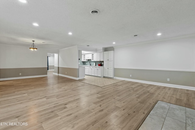 unfurnished living room featuring ornamental molding, light hardwood / wood-style flooring, a textured ceiling, and sink