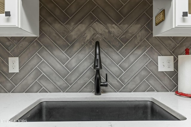 room details featuring sink, white cabinetry, and backsplash