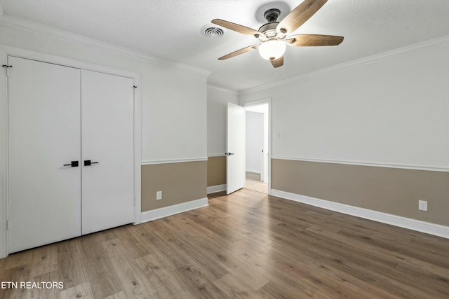 unfurnished bedroom featuring a textured ceiling, light hardwood / wood-style floors, a closet, crown molding, and ceiling fan