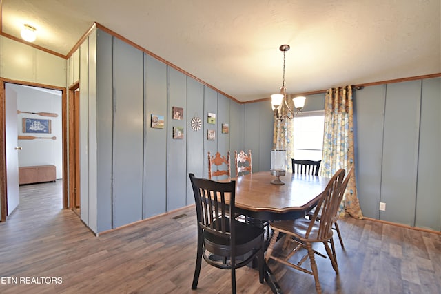 dining space with hardwood / wood-style floors, crown molding, and an inviting chandelier