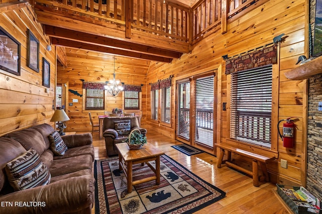 living room with wood walls, a chandelier, light hardwood / wood-style floors, and beamed ceiling