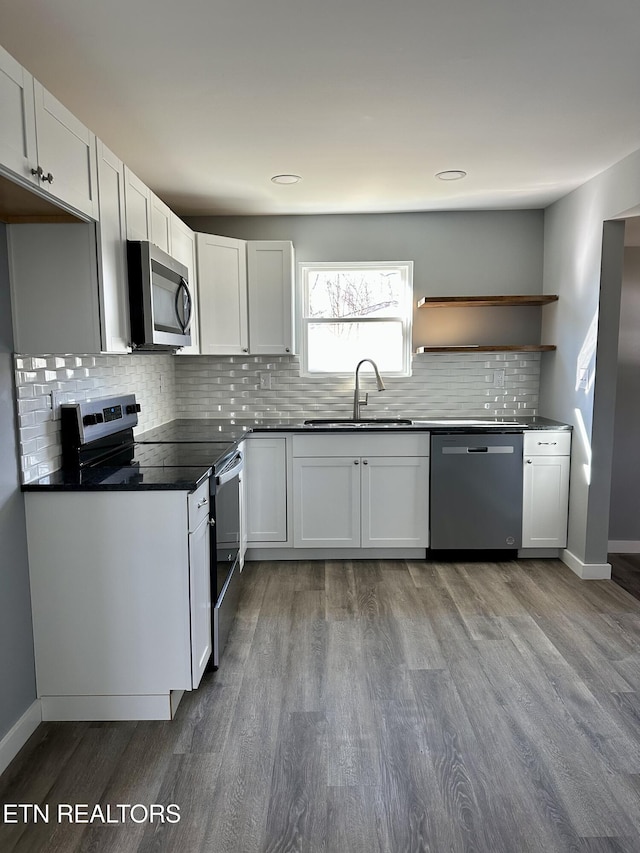 kitchen with hardwood / wood-style floors, appliances with stainless steel finishes, sink, white cabinetry, and tasteful backsplash