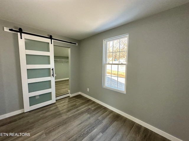 unfurnished bedroom featuring a closet, baseboard heating, a barn door, and dark hardwood / wood-style floors