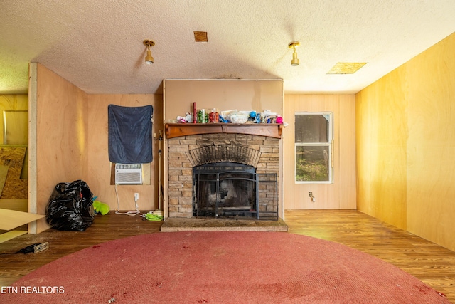 living room with a textured ceiling, wood-type flooring, wood walls, cooling unit, and a stone fireplace