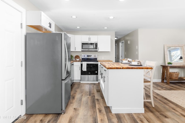 kitchen with hardwood / wood-style flooring, appliances with stainless steel finishes, white cabinetry, a kitchen bar, and wood counters