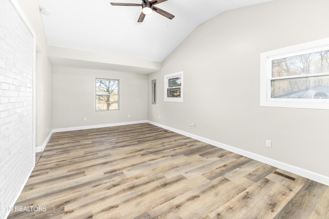 unfurnished room featuring ceiling fan, vaulted ceiling, wood-type flooring, and brick wall