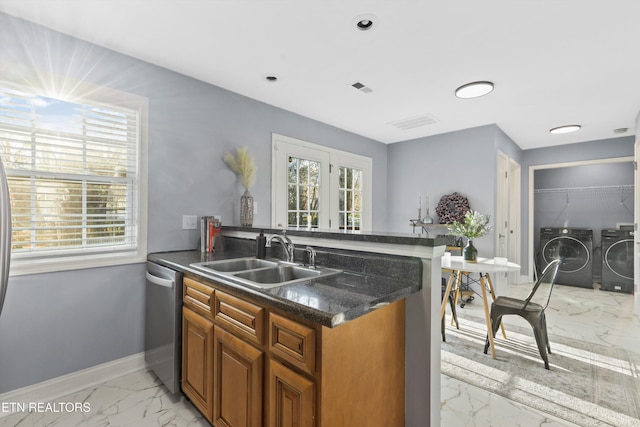 kitchen with kitchen peninsula, dark stone counters, washing machine and dryer, stainless steel dishwasher, and sink