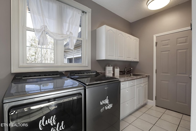 clothes washing area with sink, cabinets, washer and dryer, a textured ceiling, and light tile patterned flooring