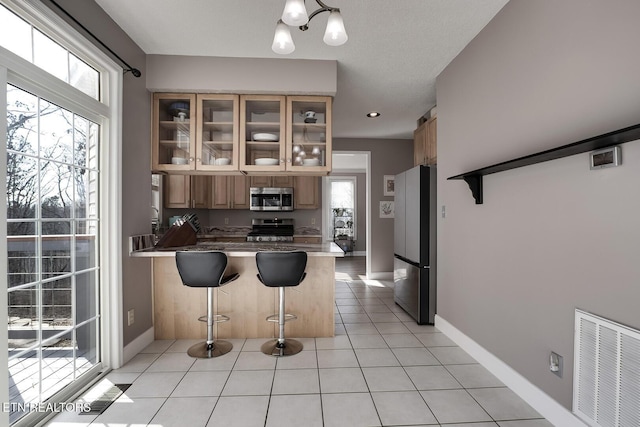 kitchen with appliances with stainless steel finishes, kitchen peninsula, a breakfast bar area, and light tile patterned floors