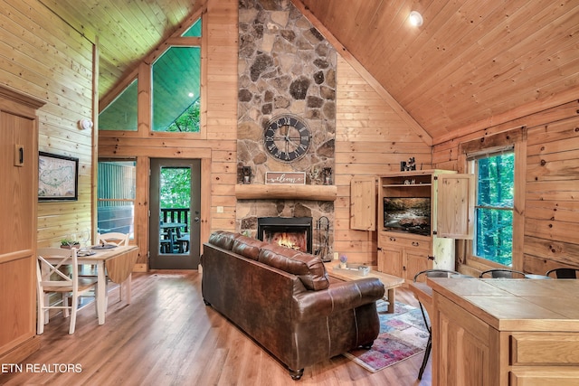 living room with a stone fireplace, wood ceiling, wooden walls, and high vaulted ceiling