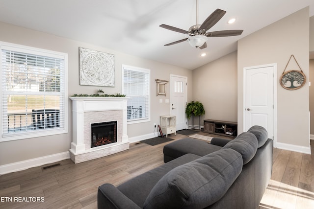 living room featuring lofted ceiling, ceiling fan, a stone fireplace, and hardwood / wood-style floors