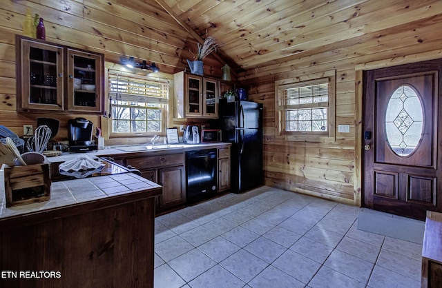 kitchen featuring vaulted ceiling, wood walls, tile counters, black appliances, and light tile patterned floors