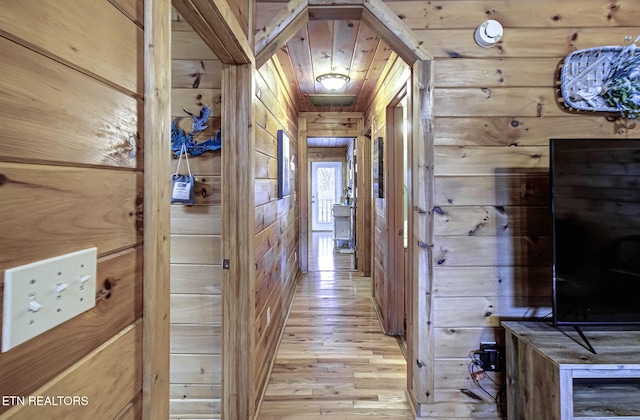 hall with light hardwood / wood-style floors, wooden ceiling, and wooden walls