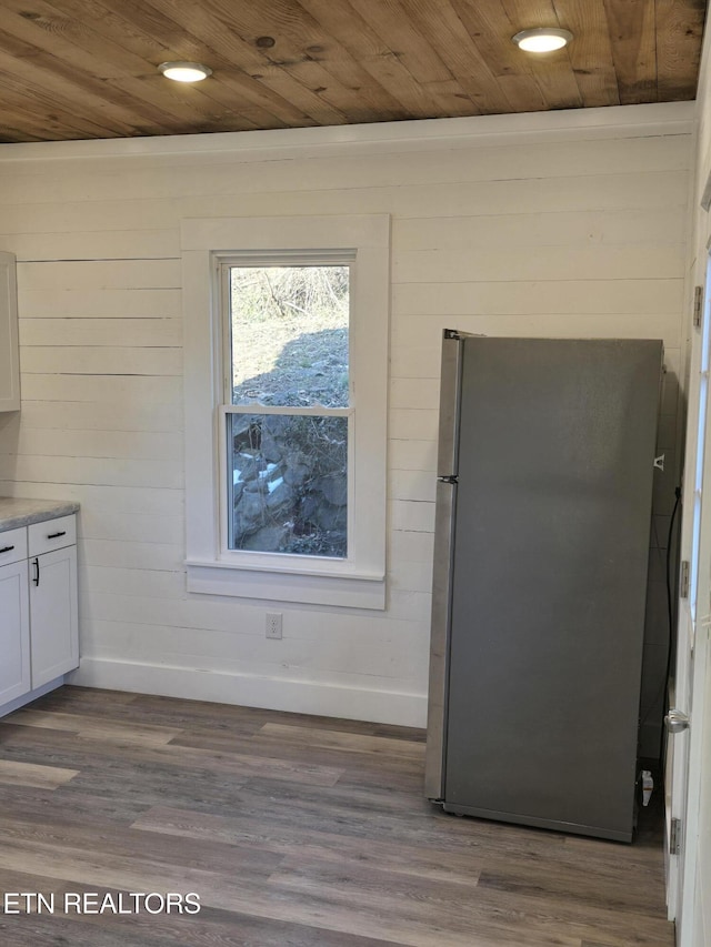 kitchen featuring wooden ceiling, stainless steel fridge, dark wood-type flooring, wooden walls, and white cabinets