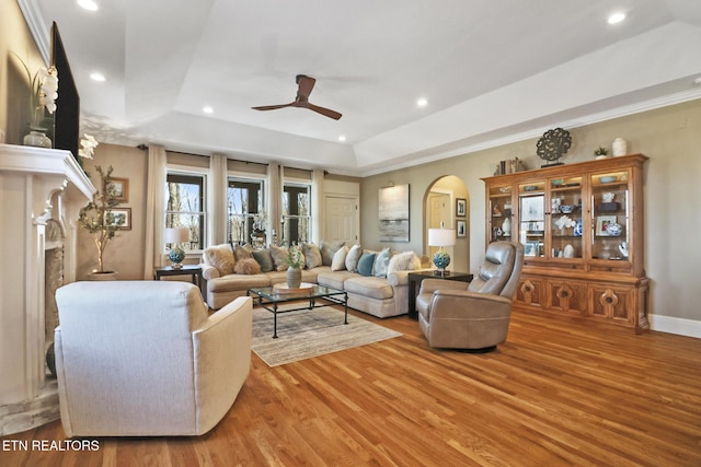 living room featuring ceiling fan, a fireplace, ornamental molding, light hardwood / wood-style floors, and a raised ceiling