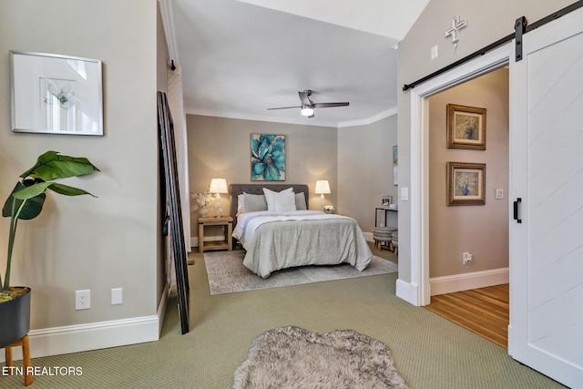 carpeted bedroom with ceiling fan, ornamental molding, and a barn door