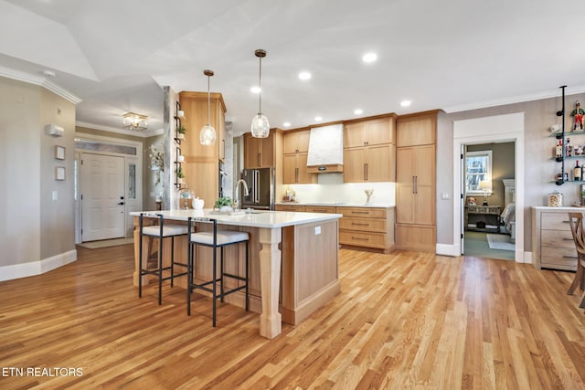 kitchen featuring premium range hood, light brown cabinetry, crown molding, hanging light fixtures, and light hardwood / wood-style floors