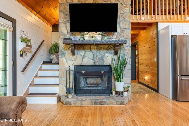 unfurnished living room featuring lofted ceiling, wood walls, light hardwood / wood-style flooring, a stone fireplace, and wooden ceiling