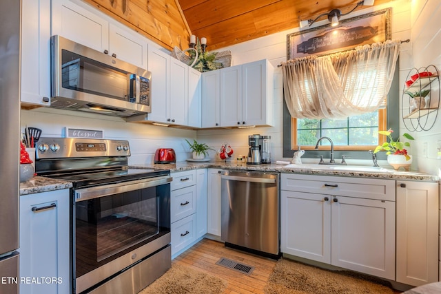 kitchen with appliances with stainless steel finishes, lofted ceiling, white cabinetry, and light stone countertops