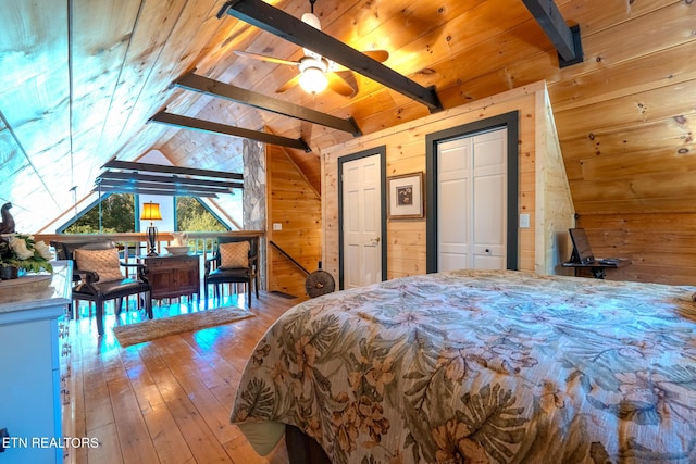 bedroom with ceiling fan, light hardwood / wood-style floors, vaulted ceiling with beams, wooden walls, and wood ceiling