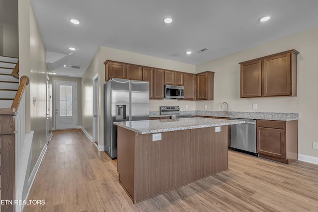 kitchen with appliances with stainless steel finishes, light hardwood / wood-style floors, light stone counters, and a kitchen island