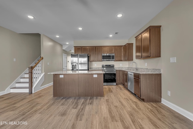 kitchen featuring a kitchen island, stainless steel appliances, light stone countertops, and light hardwood / wood-style flooring