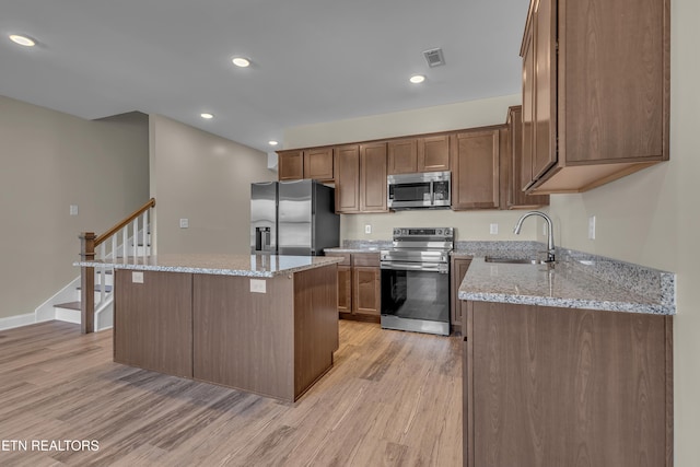 kitchen with sink, a center island, light wood-type flooring, light stone countertops, and appliances with stainless steel finishes