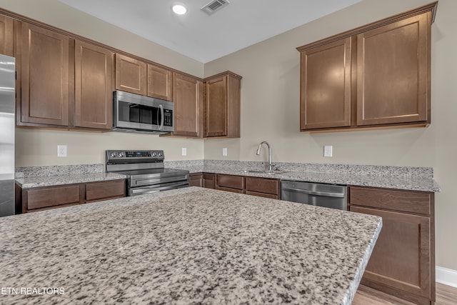 kitchen featuring stainless steel appliances, light stone countertops, light hardwood / wood-style floors, and sink